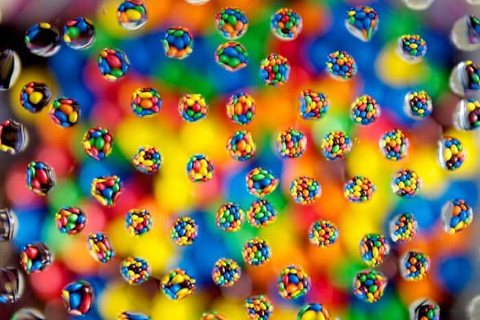A fun water droplet photography shot of circles of brightly colored sweets with droplets on a bokeh background 