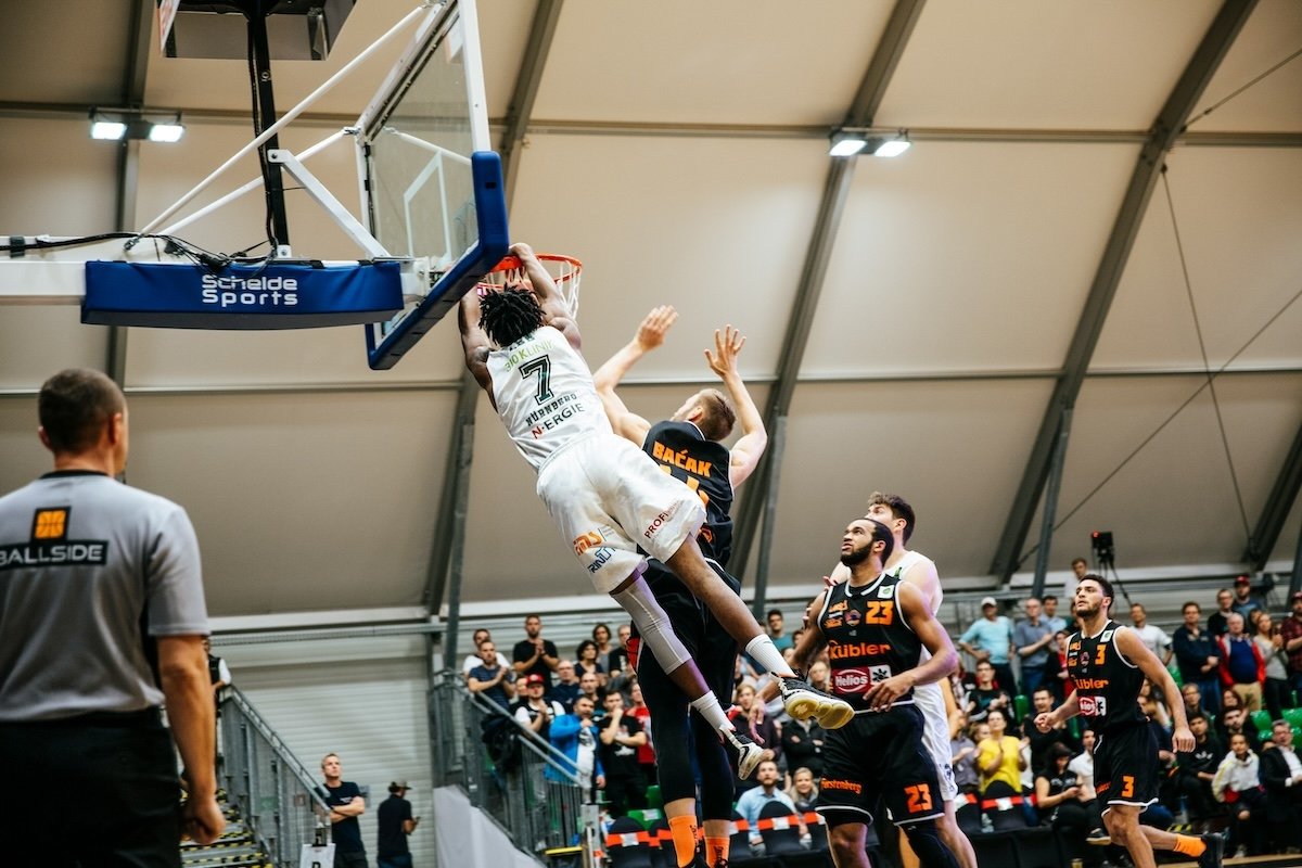 A basketball player dunking a ball over another player in a game as an example of sports photography