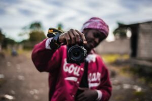 Young man in pink jacket holding a Nikon camera in front of him