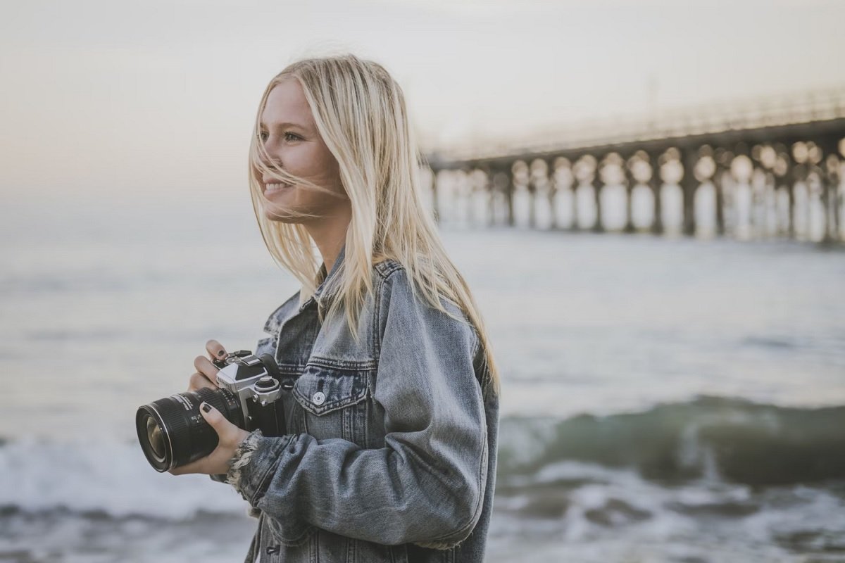 Blond young woman holding a camera on the shore