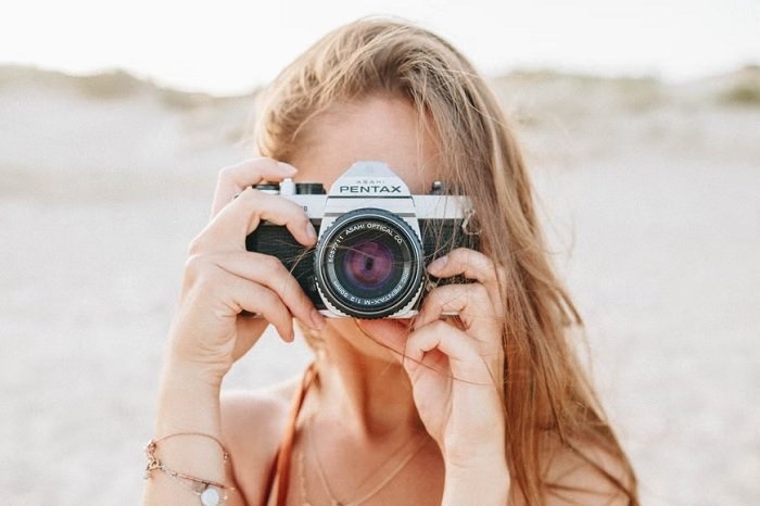 Girl on a beach holding a Pentax SLR to her face