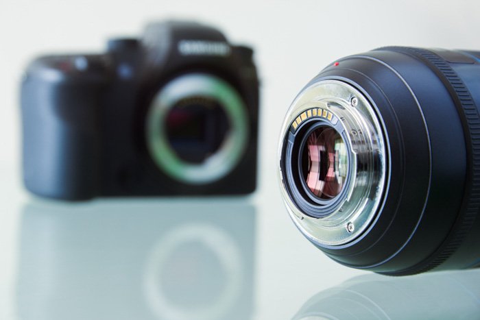 A camera lens in the foreground of a blurry dslr camera body