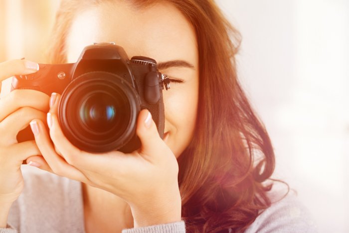 a portrait of a young woman holding a camera to her eye