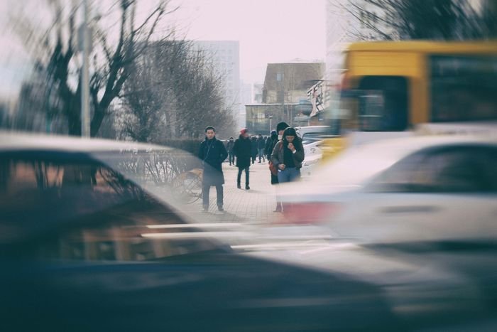 photo of pedestrians on a sidewalk with moving cars in the foreground