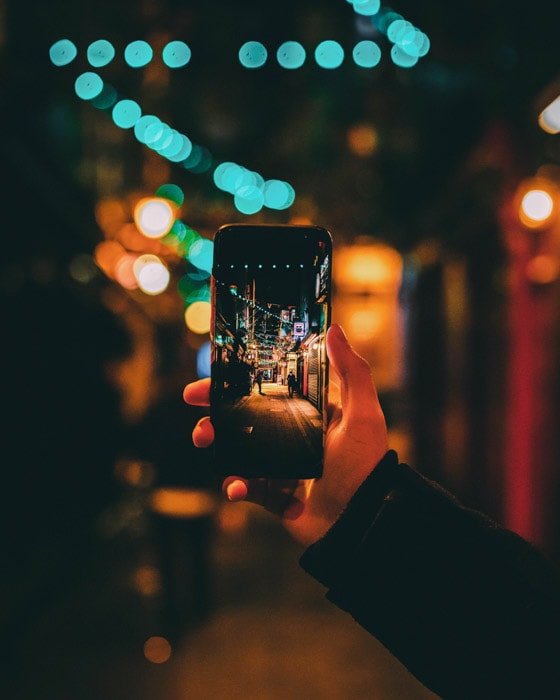 A hand holding a smartphone to naturally frame a night street photo , using a Wide and Shallow Depth of Field Together