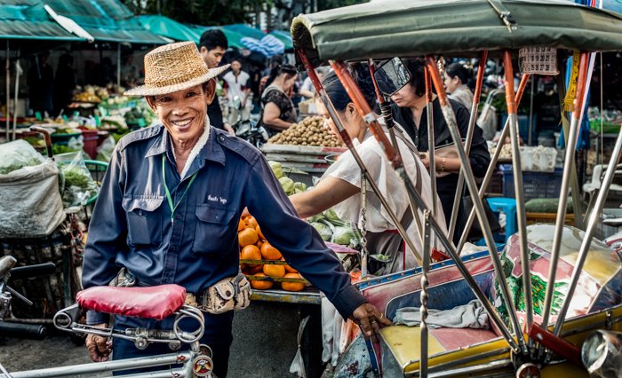 A travel documentary photograph of an Asian man at a street market