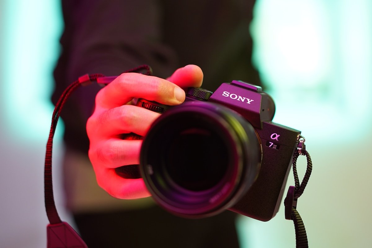 A hand holding out a Sony a7 III full-frame camera and lens