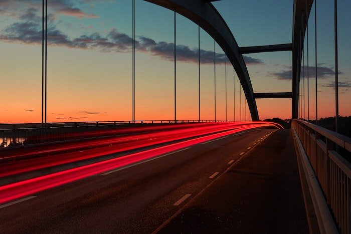 a streak of tail lights over a bridge photographed in low light