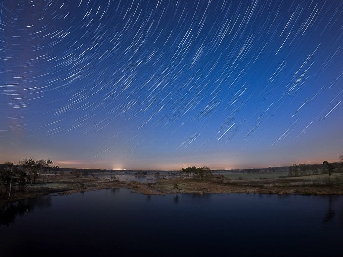Nocurnal landscape over water, creative motion blur star trails above