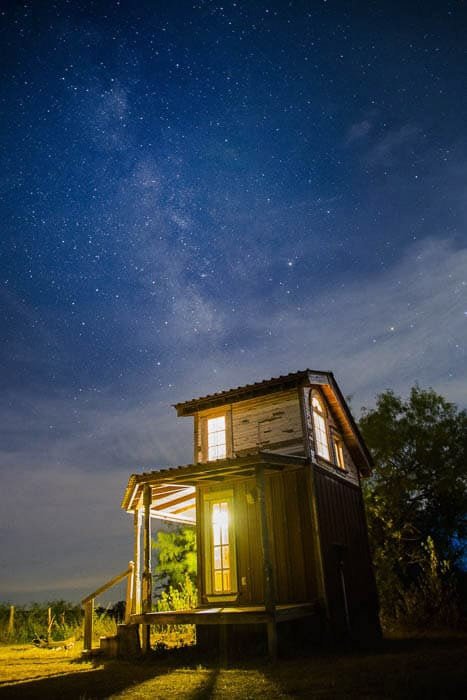 A wooden cabin taken at night in front of an impressive star filled sky