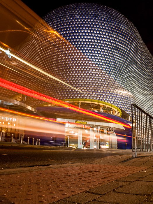 The colored motion blur of light trails in front of the Bullring shopping center in Birmingham, UK.