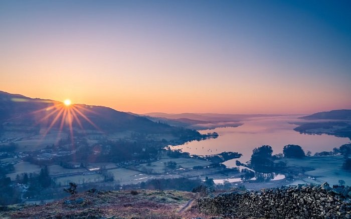 Runrise landscape with sun rising over hills across a valley near a lake