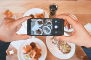 photo of hands holding a smartphone to take photo of plates of food