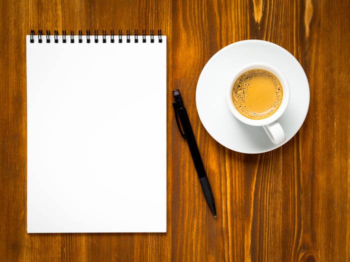 Notepad open with blank page for writing travel to-do list, a Cup of coffee and pen on the wooden brown table