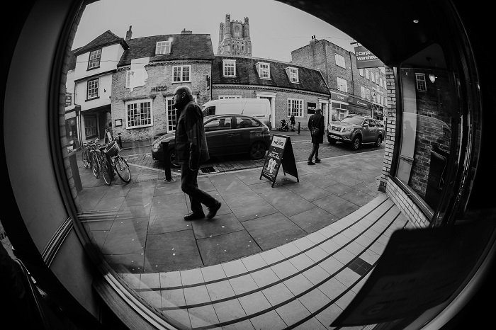 photo of man walking in the street seen through a window taken with a fisheye lens