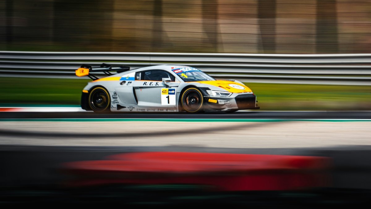 Panning shot of a race car speeding by on a race track with background motion blur