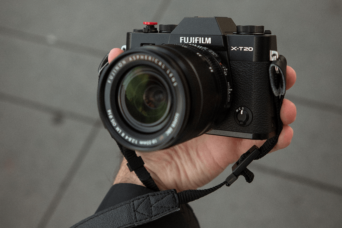 A hand holding a Fujifilm X-T20 APS-C camera and lens